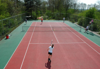 Mennesker spiller tennis på en udendørs bane omgivet af natur ved ferieparken de Bronzen Emmer i Drenthe.