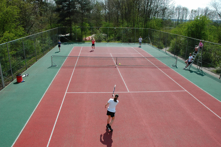Mensen spelen tennis op een buitenbaan bij vakantiepark de Bronzen Emmer in Drenthe, Nederland.