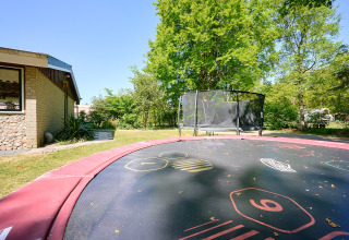 Trampolín al aire libre y casa en Holiday Resort de Bronzen Emmer, Drenthe, Países Bajos, rodeados de árboles.