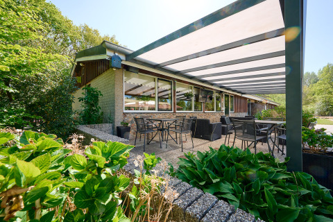 Terraza exterior cubierta con mesas y sillas en Holiday Resort de Bronzen Emmer, rodeada de vegetación en Drenthe.