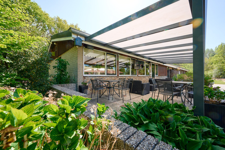Overdekt buitenterras met tafels en stoelen bij Holiday Resort de Bronzen Emmer, omgeven door groen in Drenthe.