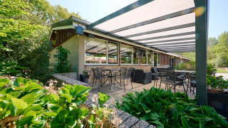 Terraza exterior cubierta con mesas y sillas en Holiday Resort de Bronzen Emmer, rodeada de vegetación en Drenthe.