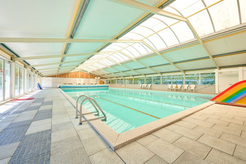 Piscina cubierta con techo de cristal, sillas y tobogán arcoíris en Holiday Resort de Bronzen Emmer, Drenthe.