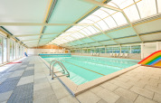 Indendørs swimmingpool med glasloft, stole og en regnbue rutsjebane i Feriepark de Bronzen Emmer, Drenthe.