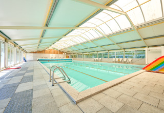 Piscina cubierta con techo de cristal, sillas y tobogán arcoíris en Holiday Resort de Bronzen Emmer, Drenthe.