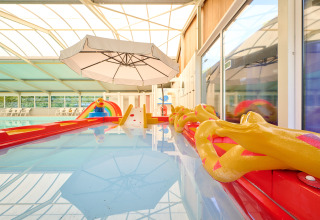 Indendørs swimmingpool med farverigt vandlegeområde og parasol i ferieparken de Bronzen Emmer i Drenthe.