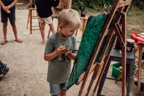 Un jeune garçon peint sur un chevalet en plein air, entouré d'enfants au Medrose Camping en France.