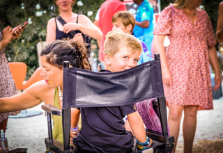 Een jongen lacht terwijl hij op een stoel zit in een levendige buitenscène op Medrose Camping, Frankrijk.