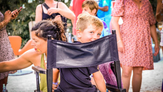 Un niño sonríe sentado en una silla en una animada escena al aire libre en Medrose Camping, Francia.
