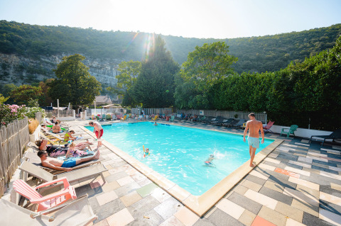Piscina al aire libre en Medrose Camping, Francia, rodeada de huéspedes relajándose y colinas verdes.