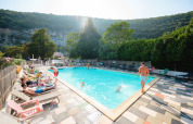 Udendørs swimmingpool på Medrose Camping, Frankrig, omgivet af bjerge og afslappende gæster i solen.