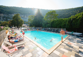 Udendørs swimmingpool på Medrose Camping, Frankrig, omgivet af bjerge og afslappende gæster i solen.