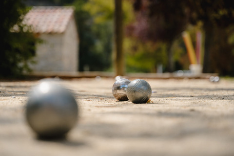 Bolas metálicas de petanca sobre grava en Medrose Camping, Auvergne-Rhône-Alpes, Francia, fondo desenfocado.