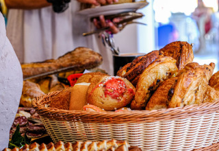 Buffettisch mit frischem Gebäck und Brot, Gäste nehmen Speisen bei Medrose Camping in Frankreich.