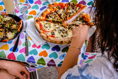 Iemand neemt een stuk pizza aan een tafel met kleurrijke hartjes bij Medrose Camping in Auvergne-Rhône-Alpes, Frankrijk.