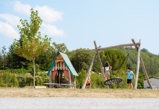 Kinderen spelen op een speelplein met schommel en huisje bij Medrose Camping in Frankrijk.