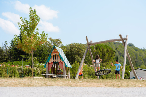 Niños juegan en un parque infantil con columpio y casita en el camping Medrose en Auvergne-Rhône-Alpes, Francia.