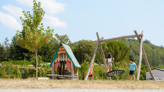 Niños juegan en un parque infantil con columpio y casita en el camping Medrose en Auvergne-Rhône-Alpes, Francia.