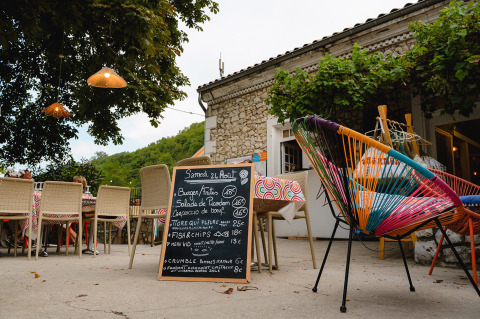 Terraza de cafetería en Medrose Camping, Francia, con sillas coloridas y menú en pizarra.