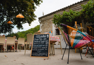 Udendørs caféområde hos Medrose Camping, Frankrig, med farverige stole og en tavle med menu.