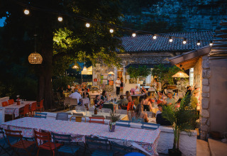 Udendørs restaurant ved Medrose Camping i Auvergne-Rhône-Alpes, Frankrig, med gæster om aftenen.