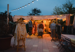 Stand de vêtements éclairé en plein air au crépuscule à Medrose Camping, Auvergne-Rhône-Alpes, France.