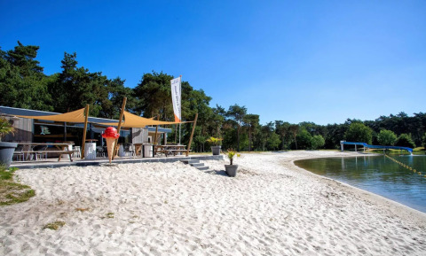 Zandstrand en eetgelegenheid aan meer bij Parc de Witte Vennen vakantiepark, Limburg, Nederland op zonnige dag.