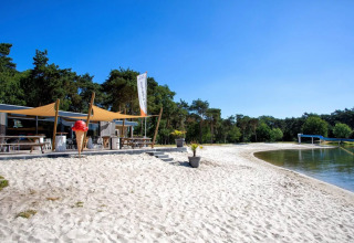 Sandy beach and lakeside dining area at Parc de Witte Vennen holiday park in Limburg, Netherlands on a sunny day.