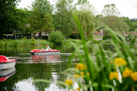 Jongen ontspant zich in een bootje op een meer omringd door groen in Parc de Witte Vennen, Limburg.