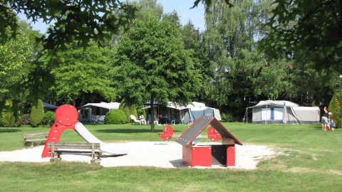 Parque infantil en Parc de Witte Vennen, Limburg, Países Bajos rodeado de tiendas y vegetación frondosa.