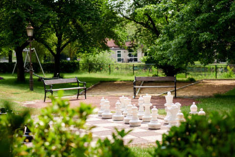 Udendørs skakbræt med store skakbrikker i en grøn park med bænke ved Parc de Witte Vennen, Limburg.