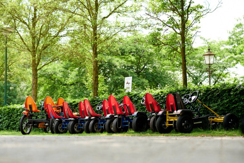Fila de coloridos karts de pedales aparcados en Parc de Witte Vennen, Limburg, Países Bajos, entre árboles.