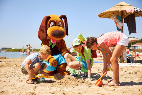 Niños juegan en la arena de la playa junto a una persona disfrazada de perro en RCN de Schotsman, Zelanda.