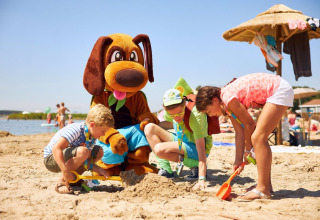 Kinder spielen am Strand im Sand mit einer Person im Hundekostüm im RCN de Schotsman, Zeeland.