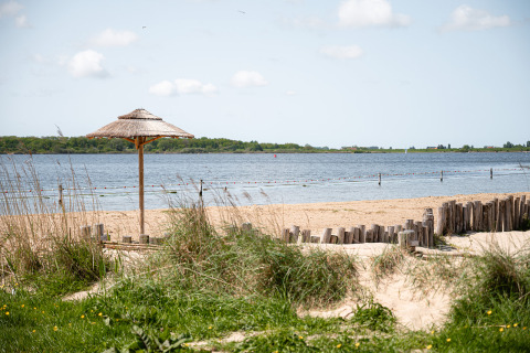 Vista de la playa en RCN de Schotsman, Zeeland, Países Bajos, con sombrilla y arena junto al lago.