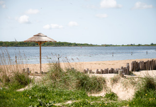 Strandzicht bij RCN de Schotsman in Zeeland, Nederland, met rieten parasol en uitzicht op het water.