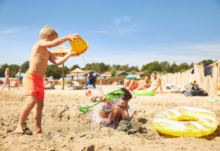 Kinderen spelen met water en zand op het strand van RCN de Schotsman, een vakantiepark in Zeeland, Nederland.