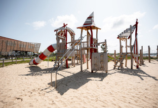 Speeltuin met houten structuur en glijbaan op zand bij RCN de Schotsman vakantiepark in Zeeland, Nederland.