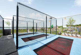 Buitentrampoline met veiligheidsnet in een vakantiepark, groen uitzicht in Zeeland zichtbaar.