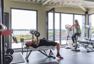 Fitnessruimte in RCN de Schotsman, Zeeland, Nederland, man traint met gewichten, vrouw op hometrainer, uitzicht.