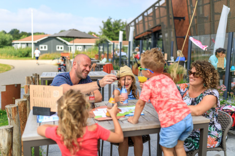 Familia disfruta de comida y bebida al aire libre en el parque vacacional RCN de Schotsman en Zelanda.