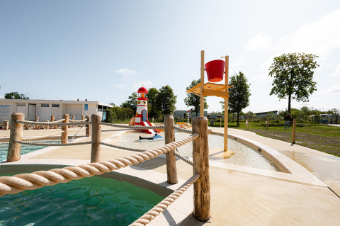 Parque acuático infantil con faro y cubo en el resort RCN de Schotsman, Zeeland, Países Bajos, en un día soleado.
