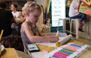 Un bambino disegna con pennarelli colorati su un tavolo in un bar con adulti sullo sfondo nelle Marche, Italia.