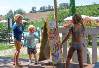 Børn i badetøj vælger is fra et skilt ved en pool i ferieparken Tenuta Tredici Ulivi, Marche, Italien.