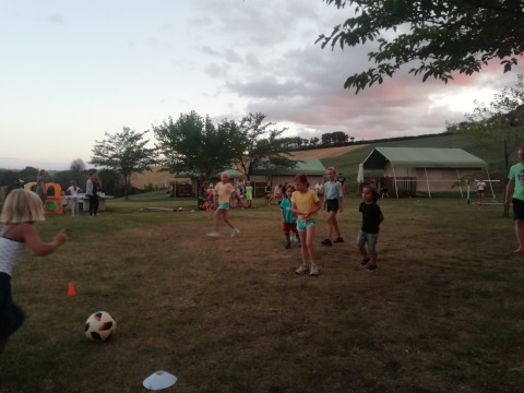 Niños jugando al fútbol en el césped del Tenuta Tredici Ulivi parque vacacional en Marche, Italia, al atardecer.