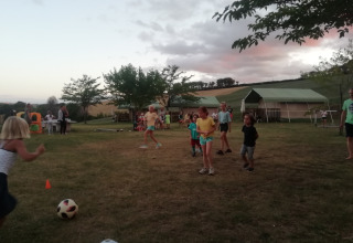 Kinder spielen Fußball auf einer Wiese im Ferienpark Tenuta Tredici Ulivi in Marche, Italien, bei Sonnenuntergang.
