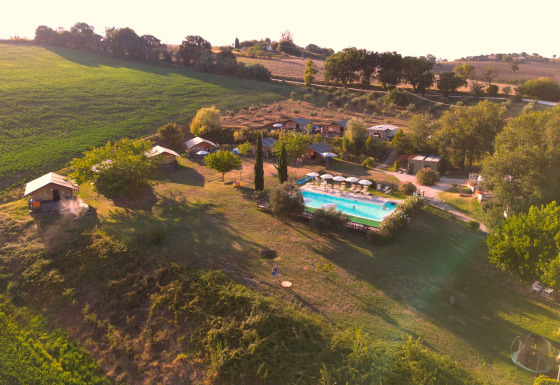 Luftfoto af Tenuta Tredici Ulivi feriepark i Marche, Italien, med swimmingpool og grønne marker.
