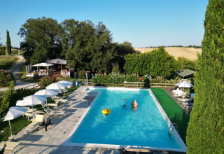 Piscina en el parque vacacional Tenuta Tredici Ulivi en Marche, Italia, rodeada de tumbonas y sombrillas.
