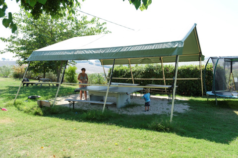 Scena all'aperto a Tenuta Tredici Ulivi con tavolo da ping pong, tenda e persone che si rilassano al sole.