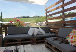 Udendørs lounge med grå sofaer, farverige puder, og en kat, på ferieparken Tenuta Tredici Ulivi i Marche, Italien.